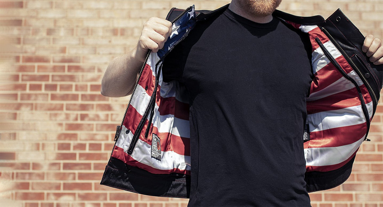 Club style with banded collar, covered snaps and cropped center zipper. Two buttoned chest pockets. Two buttoned slash pockets. American flag liner. Red Stitch. Two concealed carry pockets with tapered holsters (quick access on left hand side). Interior cellphone pocket. Single back panel. Satin lining with easy access panels for patches and embroideries.
